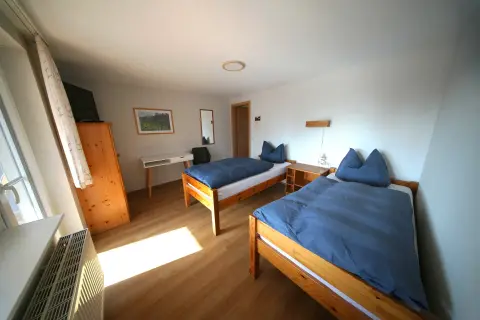 Balkonzimmer – Zwei Einzelbetten mit Holzmöbeln und Sonnenlicht