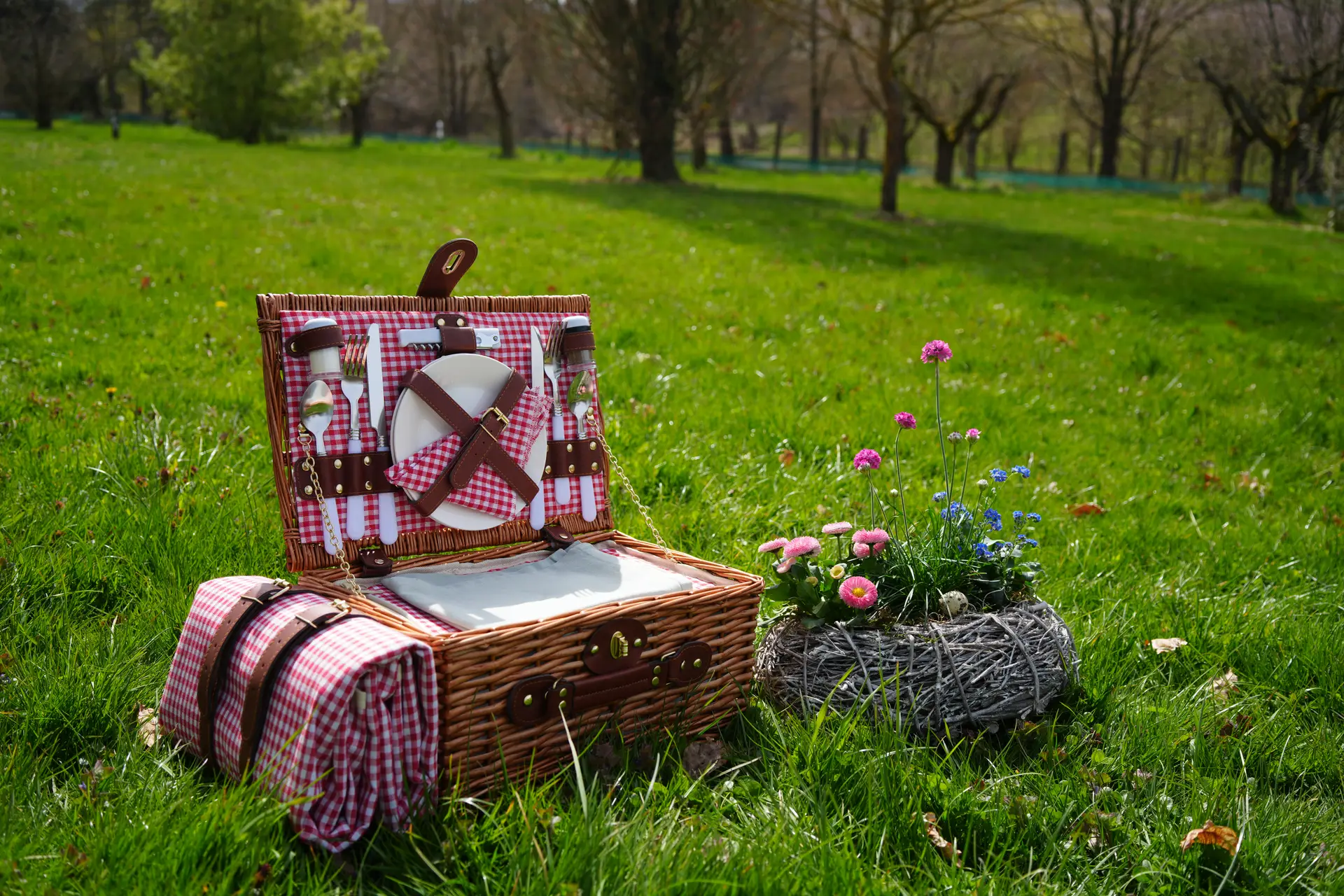 Picknickkorb mit Geschirr und Blumen auf der Wiese